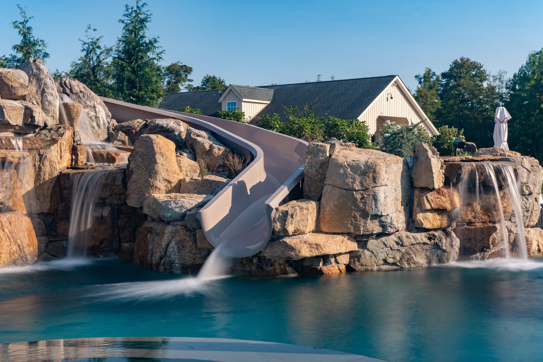 Multi-tiered natural stone boulder waterfalls cascading into a pool with a slide and lush plants