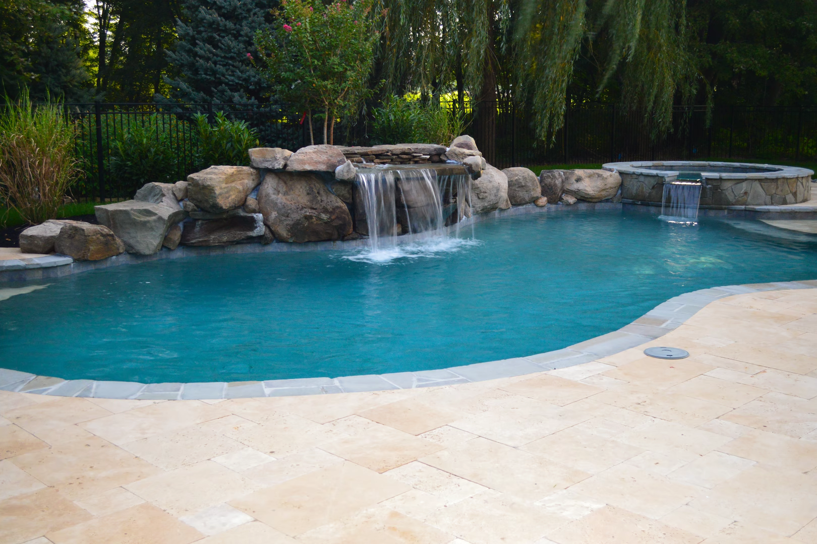 Natural stone boulder waterfall cascading into a freeform pool surrounded by lush greenery