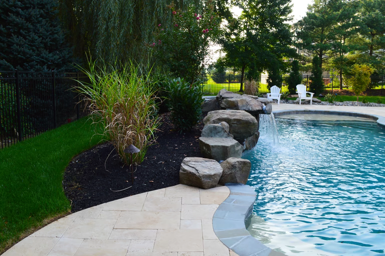 Natural stone boulder waterfall cascading into a clear pool surrounded by lush landscaping