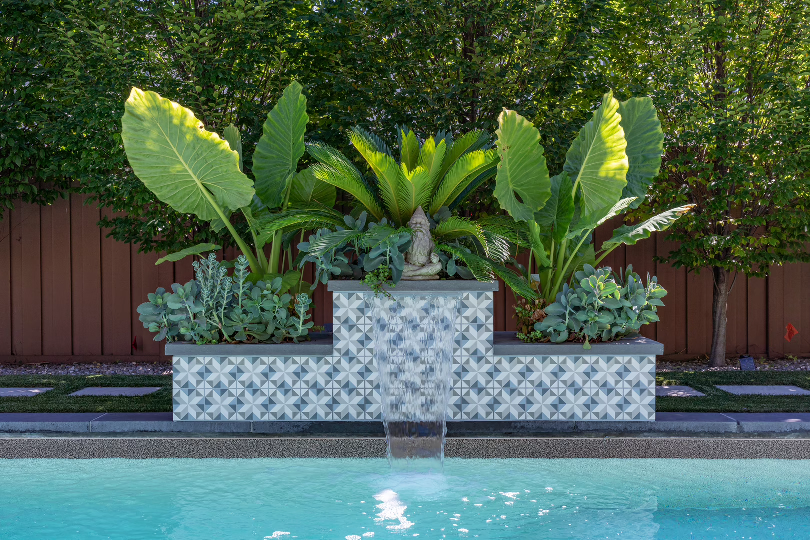 Geometric tiled waterfall spilling into a pool surrounded by lush tropical greenery