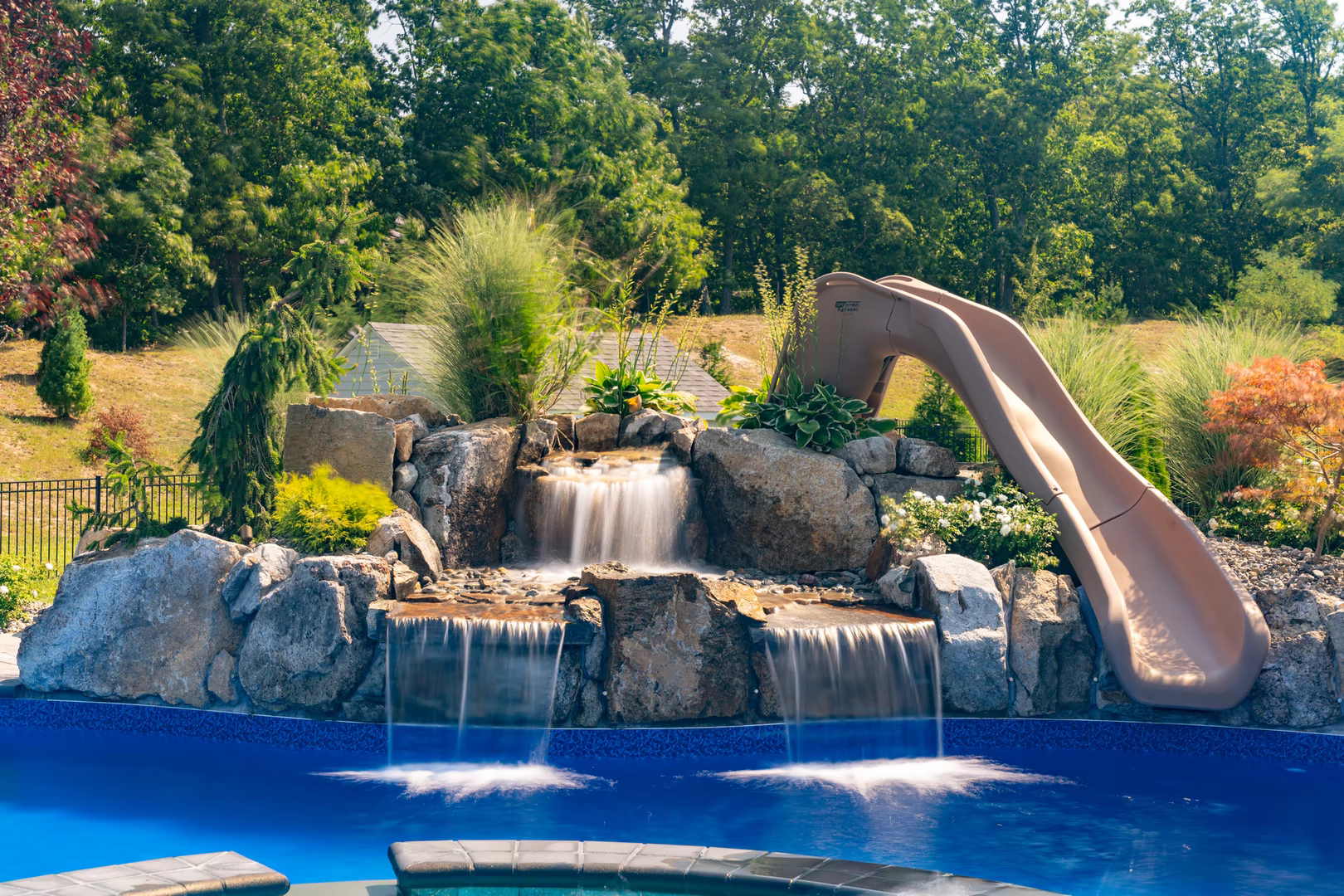 Natural stone boulder waterfalls cascading into a blue pool surrounded by lush greenery