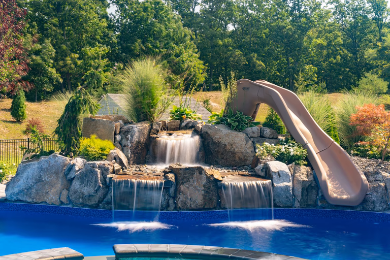 Natural stone boulder waterfalls cascading into a blue pool surrounded by lush greenery