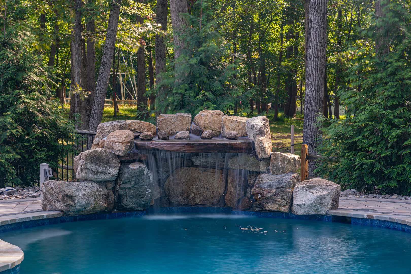 Natural stone boulder waterfall cascading into a pool surrounded by lush green trees
