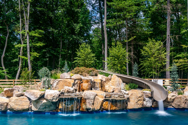 Natural stone boulder waterfall cascading into a pool surrounded by lush forest greenery