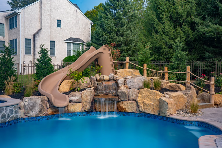 Natural stone boulder waterfall cascading into a pool surrounded by lush garden plants