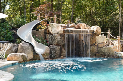 Josephine B - Mays Josephineng, NJ - This professionally installed outdoor feature combines a natural stone waterfall with a built-in slide, creating a unique water play area. The waterfall uses large, irregularly shaped boulders as the cascade structure, with multiple tiers of water flowing into a gunite pool below. The slide is seamlessly integrated into the rock formation, allowing users to descend directly into the pool water. The surrounding area features additional landscaping with shrubs and trees, enhancing the natural, resort-like atmosphere of this backyard oasis in Mays Josephineng, NJ.
