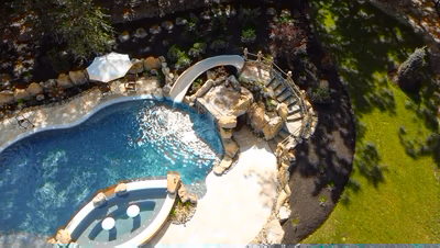 Josephine F - Mays Josephineng, NJ - This professionally installed outdoor feature combines a natural stone waterfall with a gunite pool in a serene backyard setting. The waterfall, constructed from large, irregularly shaped boulders, creates a multi-tiered cascade that flows seamlessly into the pool, enhancing both aesthetics and functionality. The surrounding area features carefully placed rocks, a small slide for added play value, and lush landscaping that complements the natural stone elements, demonstrating exceptional craftsmanship and attention to detail.