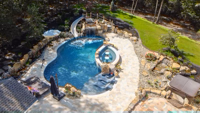 Landi G - Mays Landing, NJ - This professionally installed gunite pool features a freeform design with a prominent natural stone waterfall cascading into the main pool area. The installation includes a built-in slide leading into the water and a small spa section integrated into the pool's edge. Surrounding the pool are large boulders and carefully placed landscaping elements, creating a luxurious backyard retreat in Mays Landing, NJ.