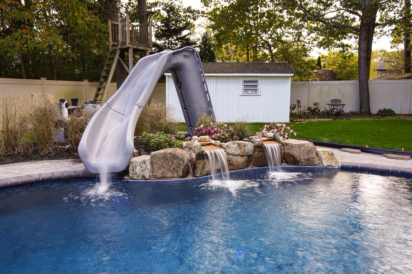 Natural stone boulder waterfalls cascading into a backyard pool surrounded by vibrant flowers