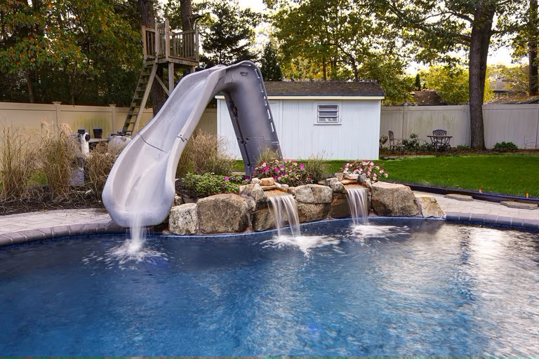 Natural stone boulder waterfalls cascading into a backyard pool surrounded by vibrant flowers