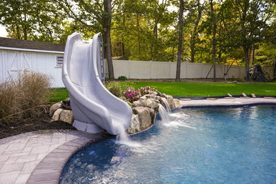 Nancy C - Lanoka Harbor, NJ - This professional installation features a custom concrete slide waterfall seamlessly integrated into a gunite pool. The waterfall's smooth concrete surface creates a dynamic cascade that flows over natural stone boulders into the deep blue pool below. The project demonstrates exceptional craftsmanship with precise concrete forming and natural stone accents that blend seamlessly with the surrounding landscaping, creating a luxurious backyard oasis in Lanoka Harbor, NJ.