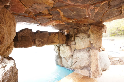 Ndakaini H - Owings Mill, MD - This custom installation features a natural stone grotto with a prominent waterfall cascading into a gunite swimming pool. The structure uses large, irregularly shaped boulders and flagstone to create an organic, rustic aesthetic. The craftsmanship is evident in the seamless integration of the waterfall and pool, with the stone walls extending to form a protective overhang above the water.