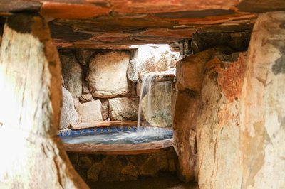 Sefinen K - Finksburg, MD - This custom installation features a natural stone waterfall cascading gracefully into a gunite pool, framed by large, rugged boulders that create a rustic, grotto-like ambiance. The waterfall's tiered design showcases skilled craftsmanship, with water flowing smoothly over carefully placed stones. The pool itself is integrated seamlessly into the surrounding stonework, enhancing the natural, outdoor living environment in Finksburg, MD.
