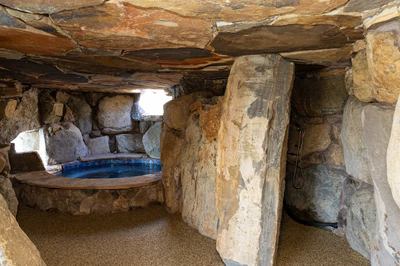 Sefinen L - Finksburg, MD - This custom indoor pool features rough-hewn natural stone walls and ceiling creating a rustic grotto atmosphere. The pool itself appears to be constructed with durable gunite material and is accented by large boulders integrated into the surrounding architecture. Natural lighting streams through an opening above, enhancing the serene, cave-like ambiance of this unique indoor swimming space.