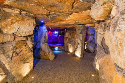 Sefinen Q - Finksburg, MD - This professionally constructed grotto features rough-hewn natural stone walls and ceiling creating an intimate, cave-like atmosphere. The centerpiece is a built-in pool with a cascading waterfall element that flows over large stone formations, enhanced by strategic blue LED lighting that accentuates the textures and creates a serene ambiance. The space demonstrates exceptional craftsmanship with seamless integration of the water feature into the stone structure, resulting in a luxurious and naturalistic outdoor living area.