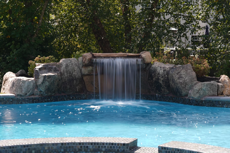 Natural stone boulder waterfall cascading into a blue pool with lush green foliage
