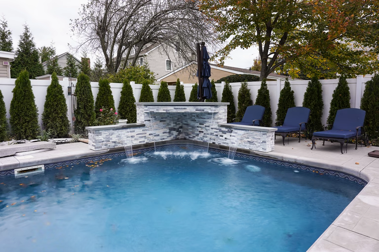 Stacked stone sheer descent waterfalls flowing into a backyard pool with evergreen landscaping