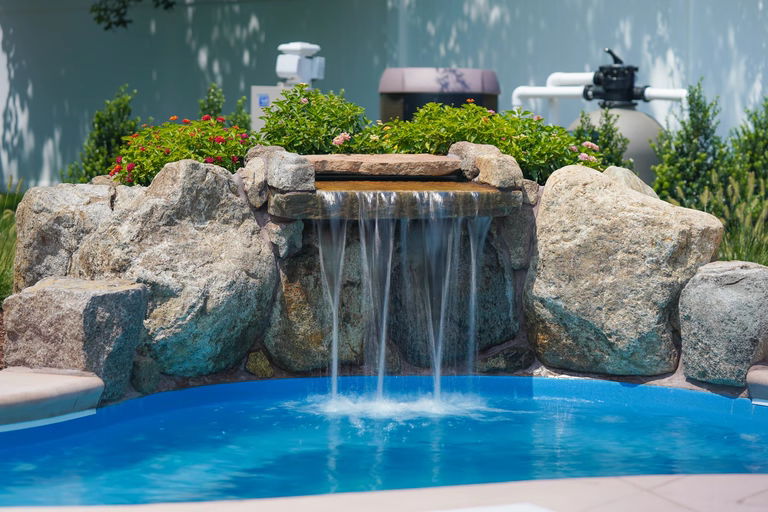 Natural stone boulder waterfall with sheer flow into pool surrounded by lush greenery