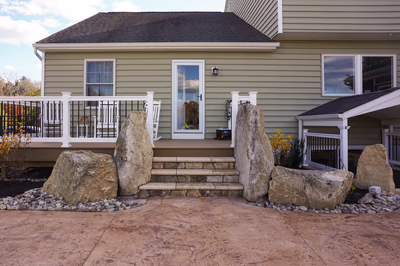 Williams T - Port Republic, NJ - This custom outdoor living project features a natural stone waterfall integrated into a patio setting. The waterfall is constructed from large, irregularly shaped boulders arranged to create a cascading water flow, surrounded by a bed of small river rocks. The surrounding patio is made of warm-toned concrete pavers, complementing the natural stone elements and providing a durable, low-maintenance surface.