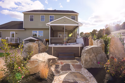 Williams V - Port Republic, NJ - This professional installation features a custom hot tub integrated into a serene backyard setting in Port Republic, NJ. The hot tub is surrounded by large, naturally occurring boulders that create a rustic, organic feel, enhancing the outdoor living space. The landscaping includes a stone pathway bordered by white pebbles and low-lying shrubs, contributing to a tranquil and well-maintained environment. The construction quality is evident in the seamless integration of the hot tub with the surrounding natural elements, creating a harmonious and inviting retreat.