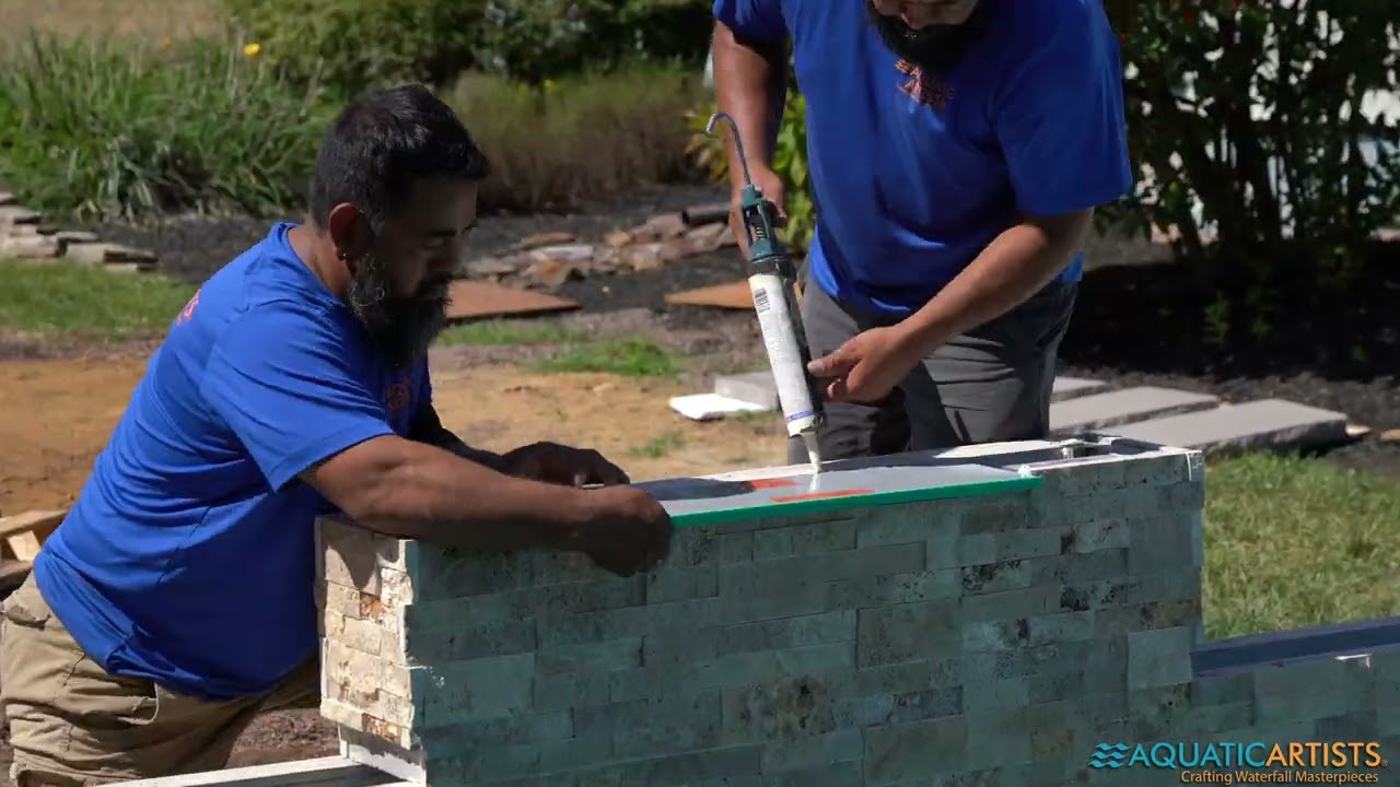 Aquatic Artists craftsmen setting stacked-stone veneer on a waterfall wall