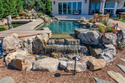 Day X - Manasquan, NJ - A backyard with a wooden deck and a waterfall surrounded by rocks and plants