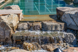 Day Y - Manasquan, NJ - A small waterfall in a rocky area next to a swimming pool.